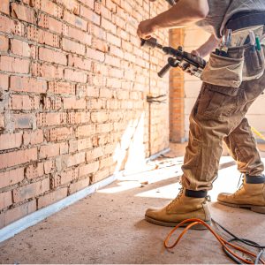 Handyman at a construction site in the process of drilling a wall with a perforator.